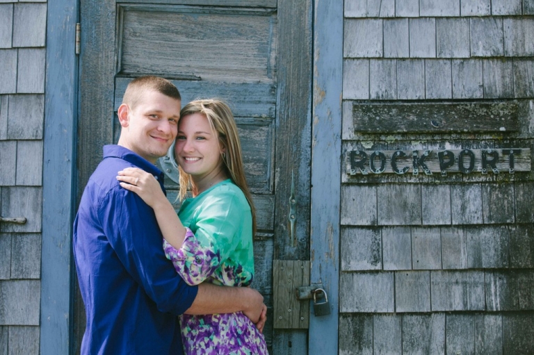 Engaged couple posing next to fishing shed with Rockport sign