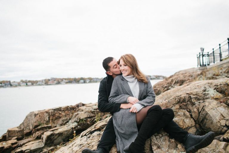 Newly engaged couple sitting on rocks in Marblehead, Massachusetts for a Marblehead Engagement shoot