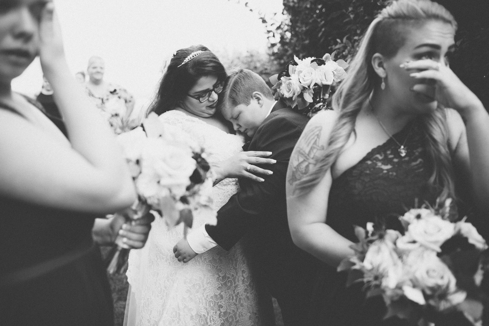 Bride hugs emotional nephew with tearful bridesmaids wiping their tears