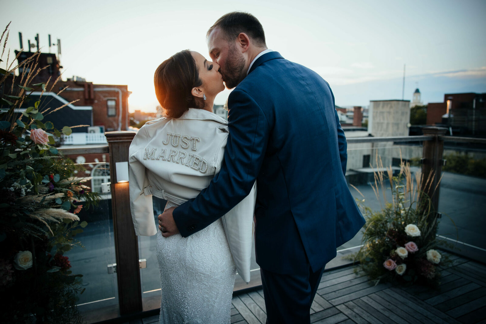 Bride and groom kiss and bride is wearing a white leather jacket with pearl lettering that reads 